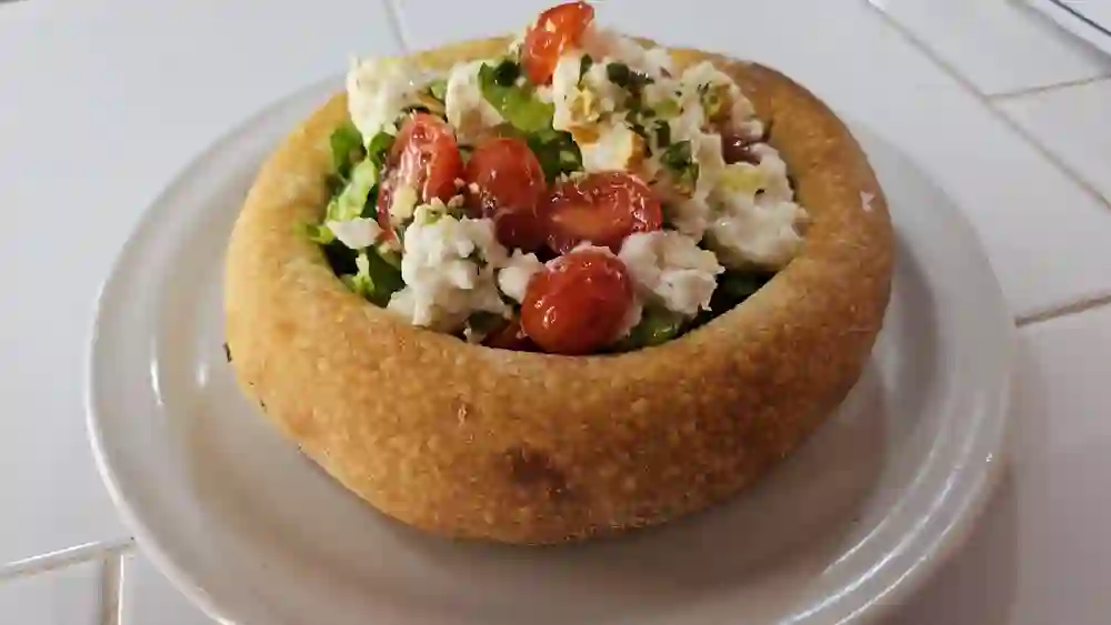 Ensalada servida dentro de un pan bowl con burrata y jitomate cherry